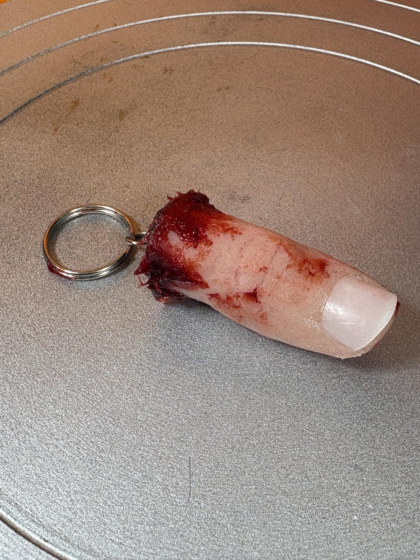 A realistic severed finger keychain with a bloody, ragged end and a white fingernail.