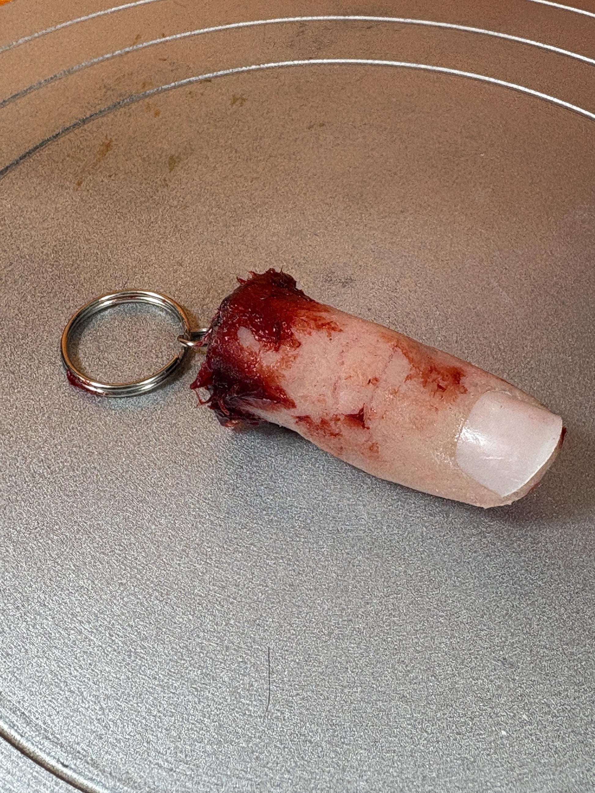 A realistic severed finger keychain with a bloody, ragged end and a white fingernail.